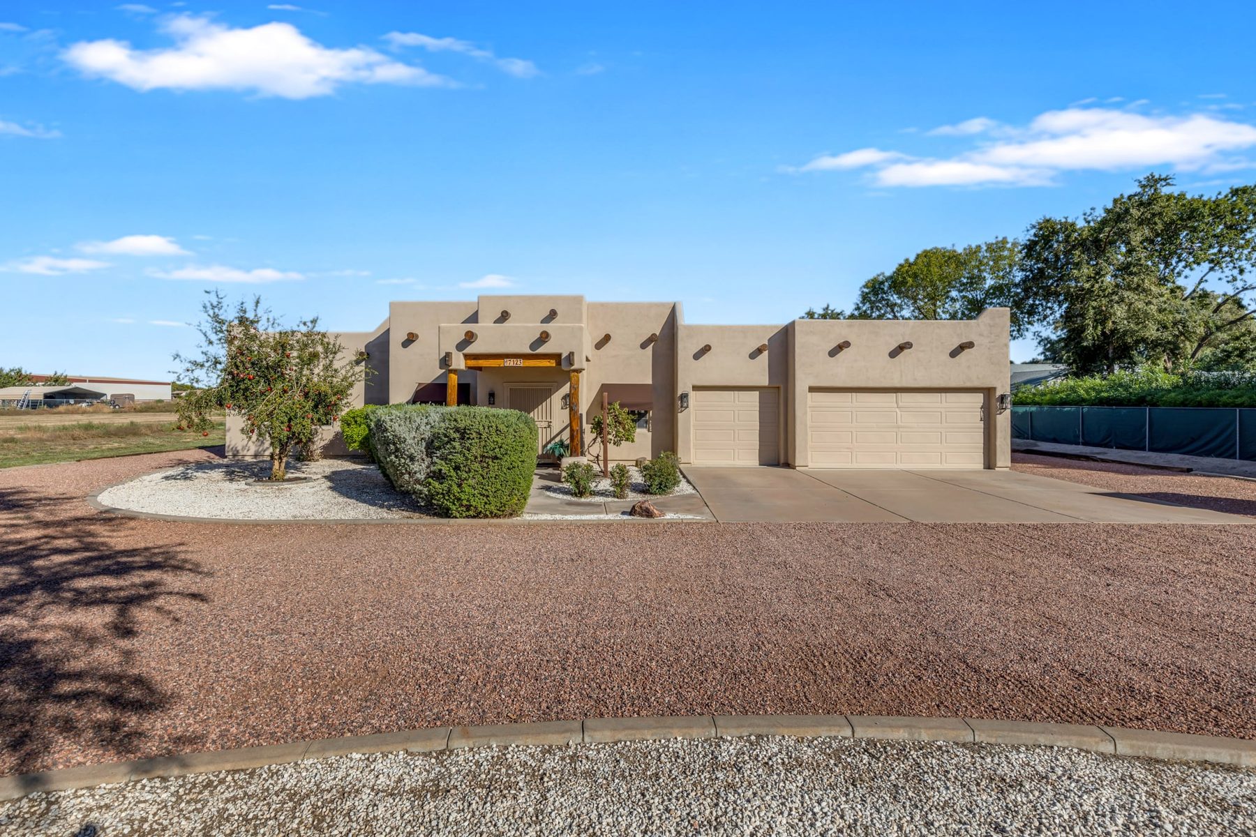 Front of the stucco Santa Fe-style home with a 3-car garage and gravel drive