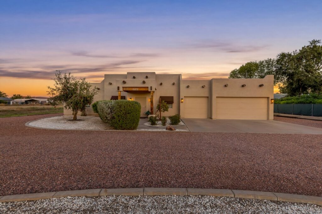 Front of the Santa Fe-style home at sunset with lit entry and 3-car garage