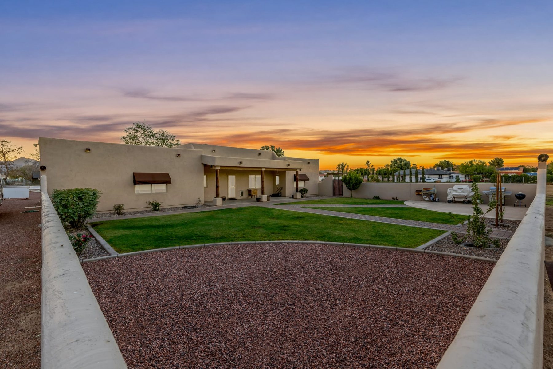 Walled backyard at sunset with grass, paver walks and covered patio